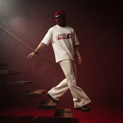 A model wearing a white graphic t-shirt and white pants walks down dark wooden stairs in a moody, red-lit environment. The model is wearing a red balaclava and sunglasses, and the shirt features a graphic that reads 'PRINT ON'.