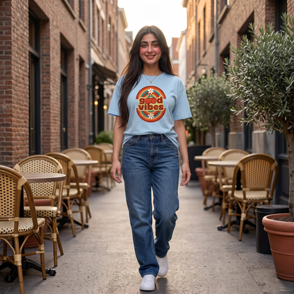 A woman walking down a brick alleyway wearing a light blue graphic t-shirt with a retro circular design that reads 'Spooktastic' and 'Good Vibes', paired with blue jeans and white sneakers.